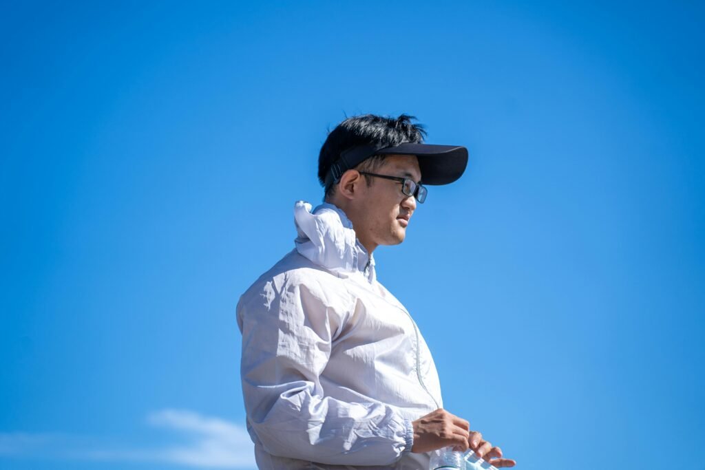 A man wearing a white jacket and cap looks into the distance against a clear blue sky.